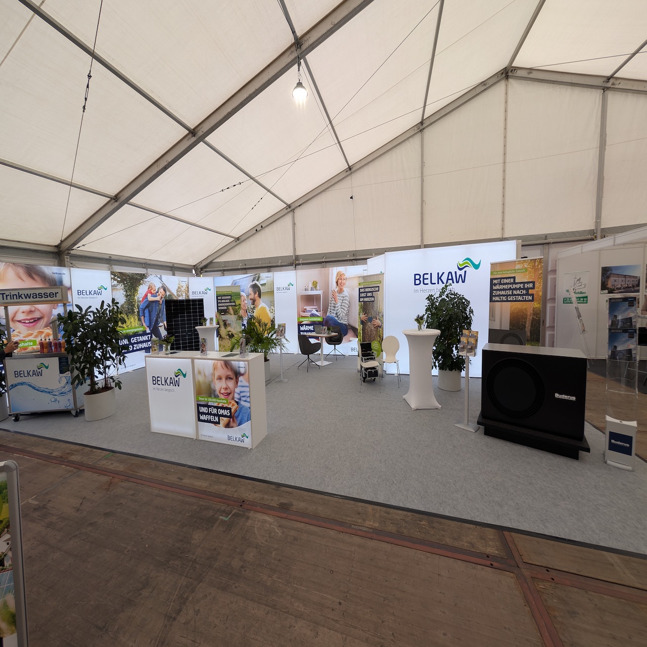 Promotionstand von der BELKAW, mit einer Trinkwassertheke, einer weiteren Theke und mehreren Rollups und bedruckten Wänden